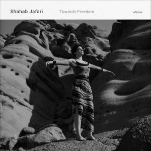 Black-and-white photograph of a dancer standing with arms outstretched among rock formations for Shahab Jafari’s composition Towards Freedom.